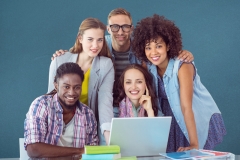 Happy classmates using laptop on table